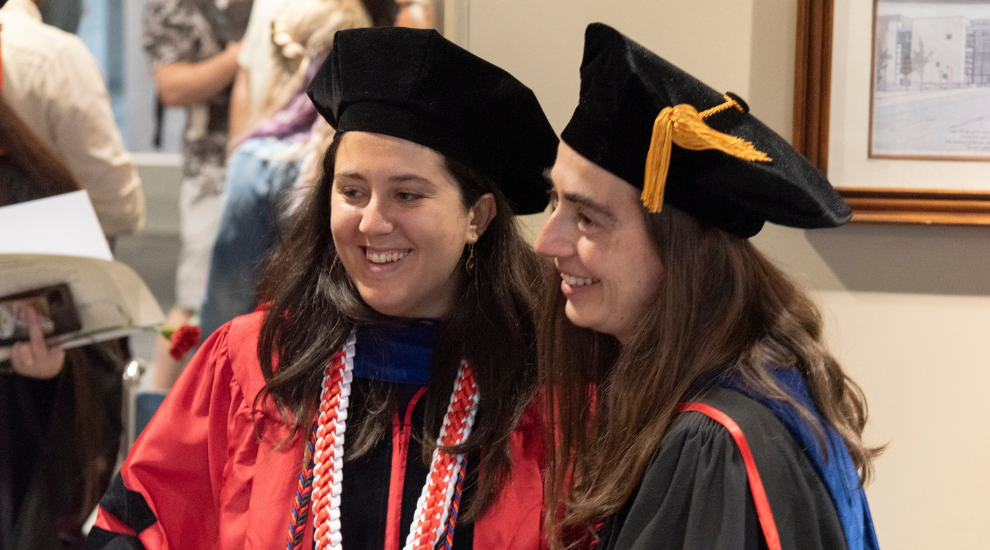 faculty and student candidly laughing in regalia during commencement